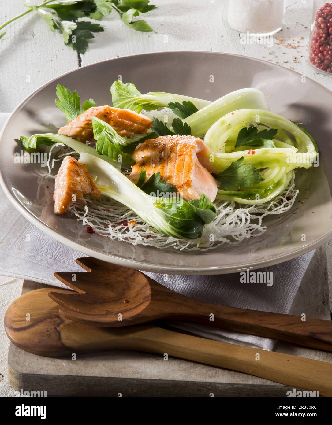 Salmon and bok choy on a bed of glass noodles on a plate with wooden cutlery Stock Photo