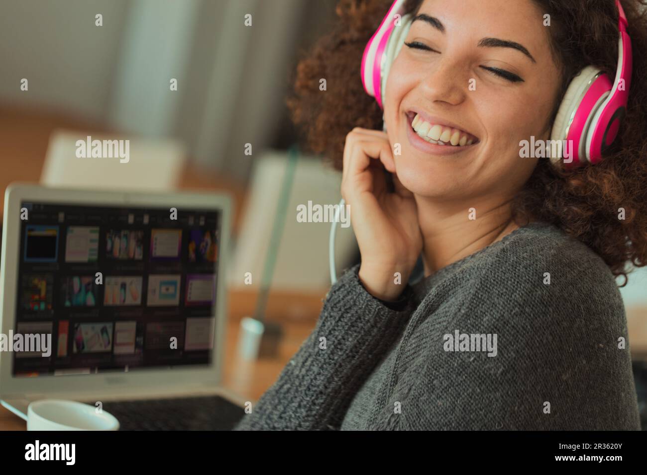 A jovial young woman with curly hair is absorbed in her pink headphones