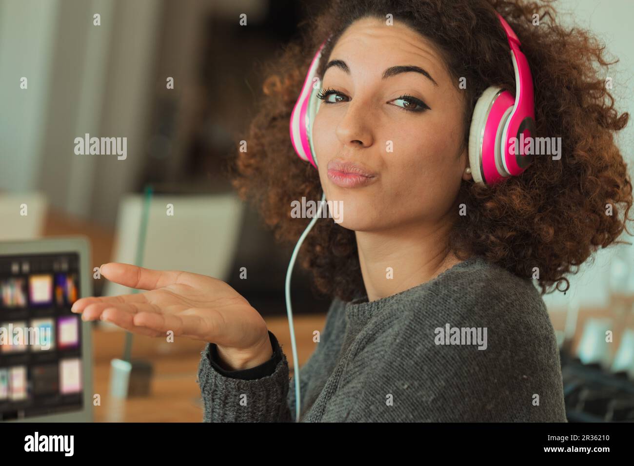 A jovial young woman with curly hair is absorbed in her pink headphones