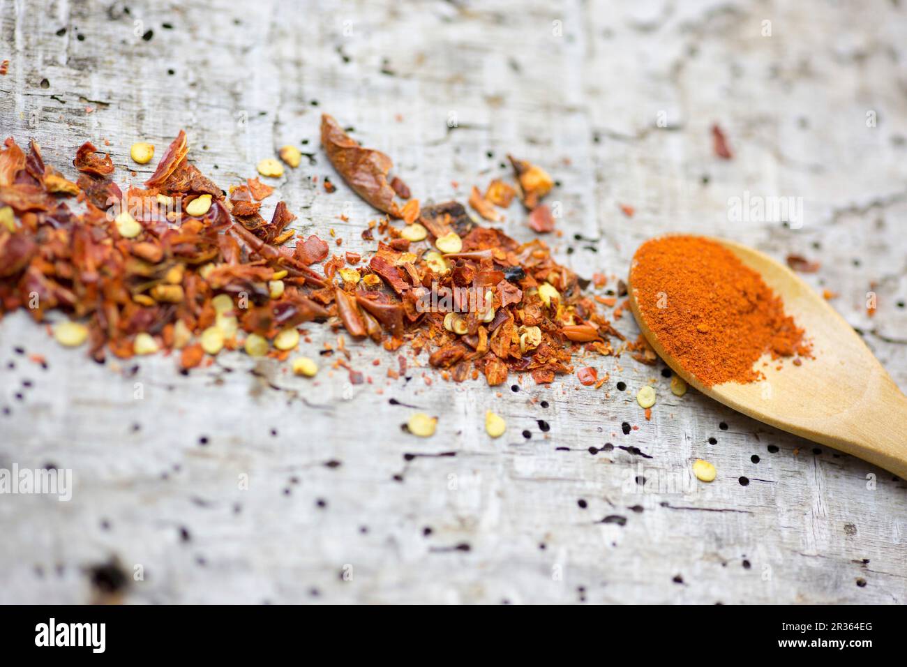 Chilli powder on a wooden spoon and chilli flakes on a wooden surface Stock Photo