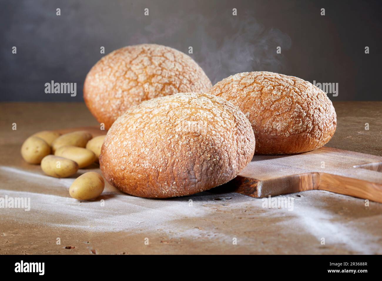 Three potato and wheat loaves with potatoes on an olive wood chopping