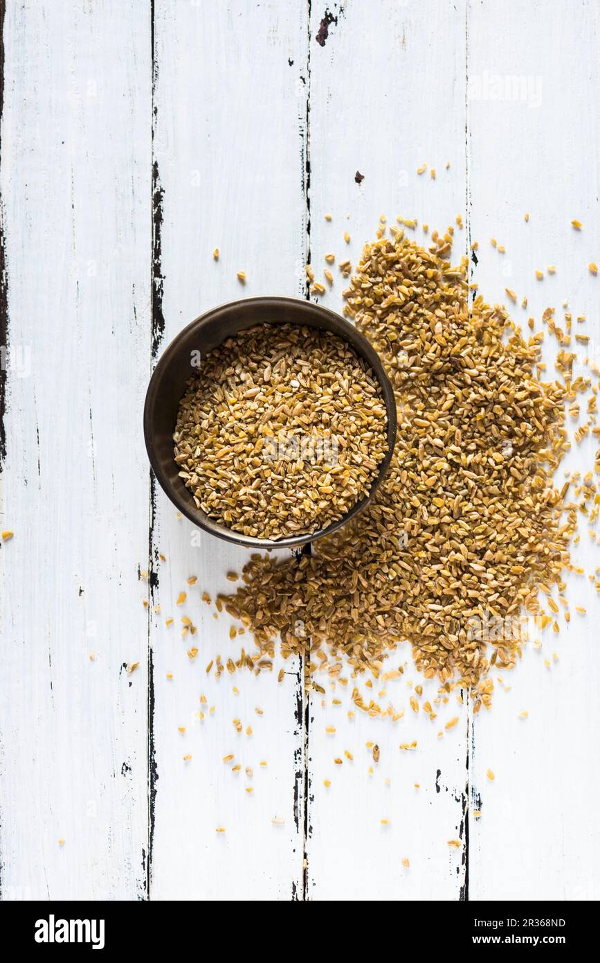 Coarsely crushed freekeh in a bowl and on a wooden surface Stock Photo
