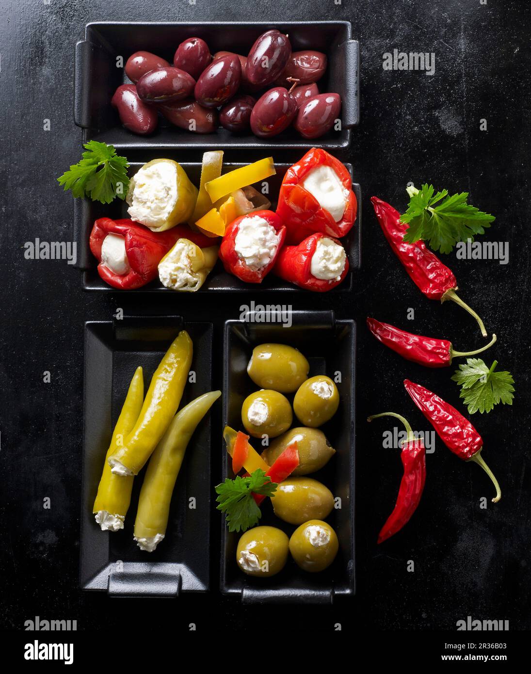 Various olives, stuffed mini peppers and jalapeños on a black baking tray Stock Photo