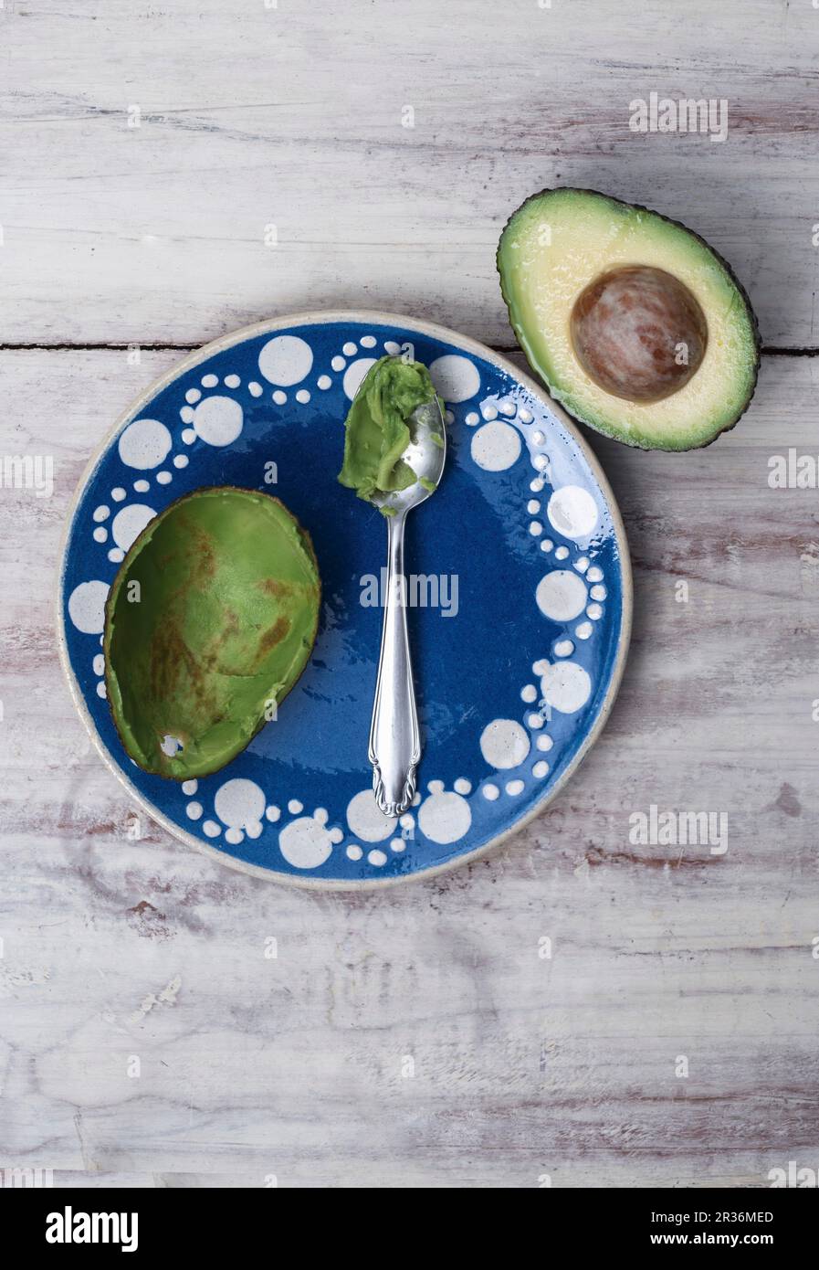 A scooped out avocado half on a blue clay plate with a spoon next to