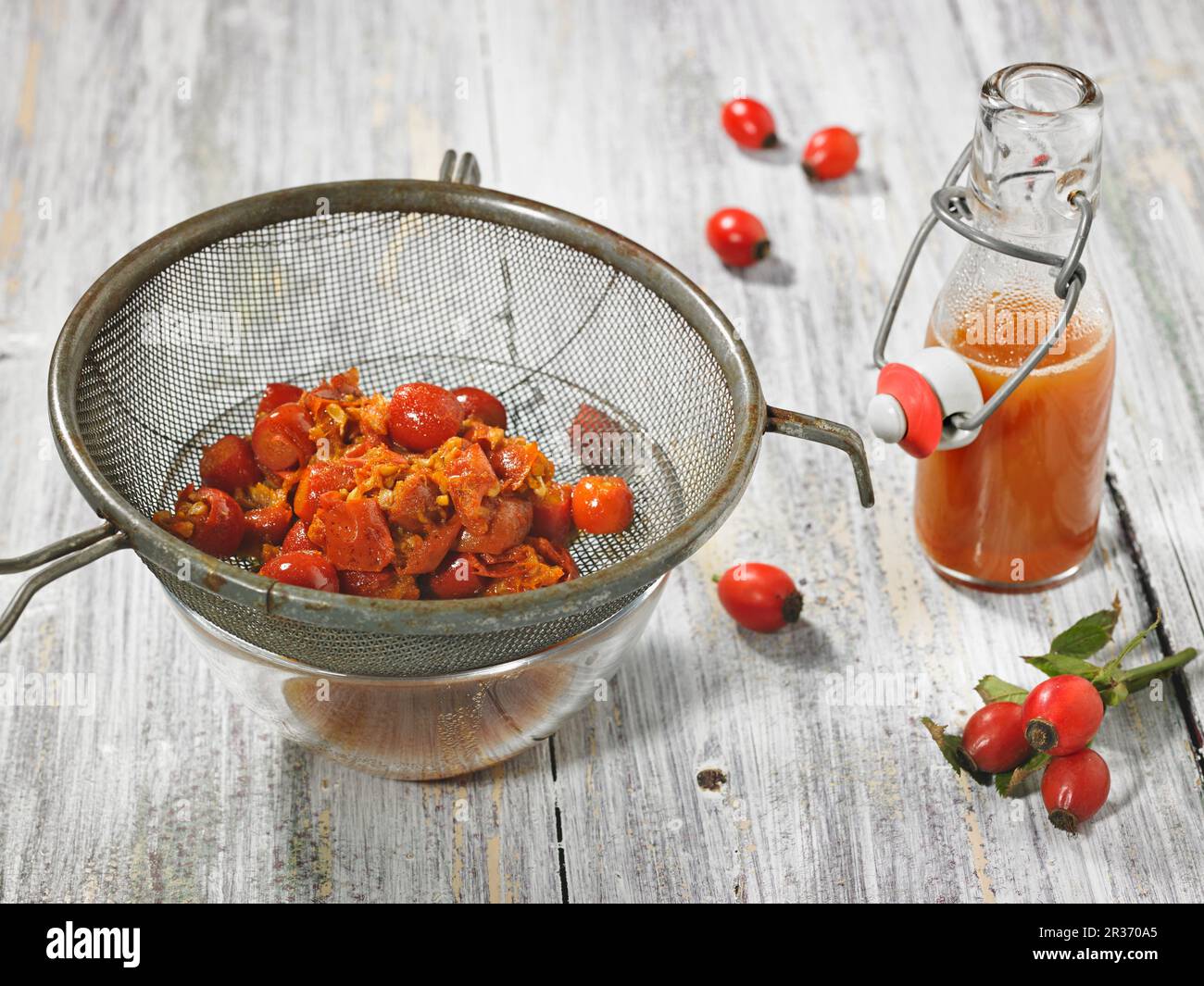 Rose hip juice in a bottle with pitted and boiled rose hips in a strainer Stock Photo Alamy