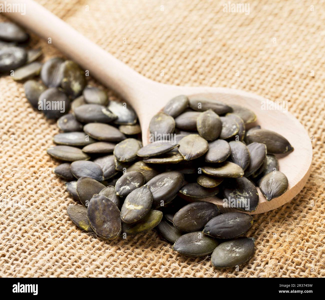 Unpeeled pumpkin seeds on a wooden spoon on a jute sack Stock Photo