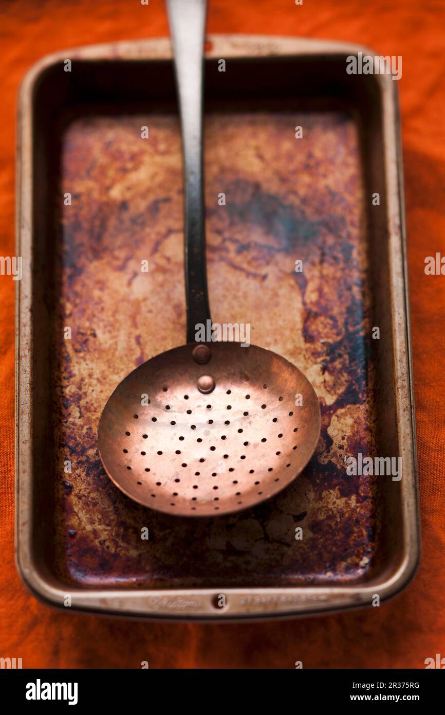 A burnt roasting tin with a strainer spoon Stock Photo Alamy