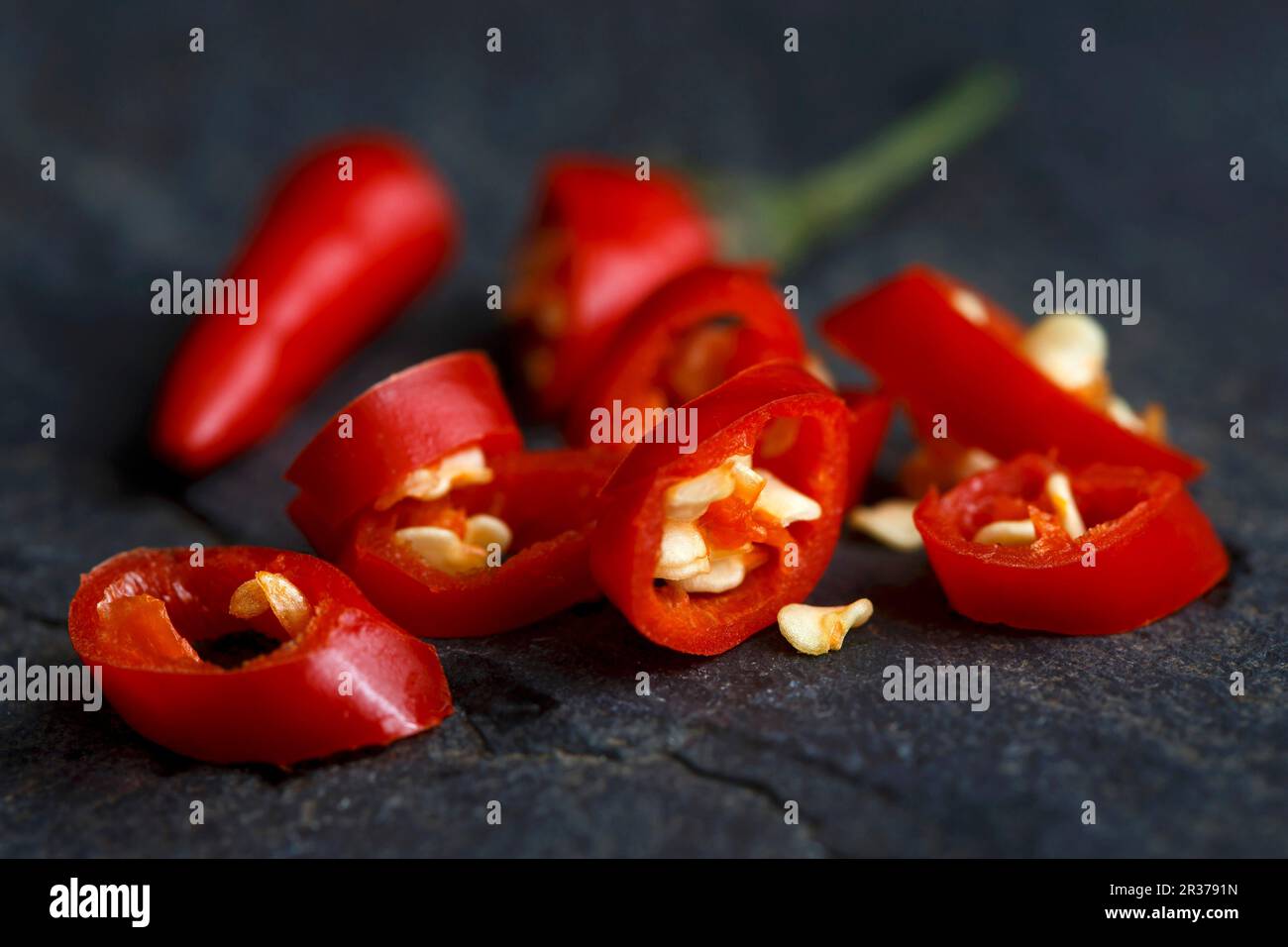 Cut fresh birds eye chilli with seeds on dark slate background. Stock Photo