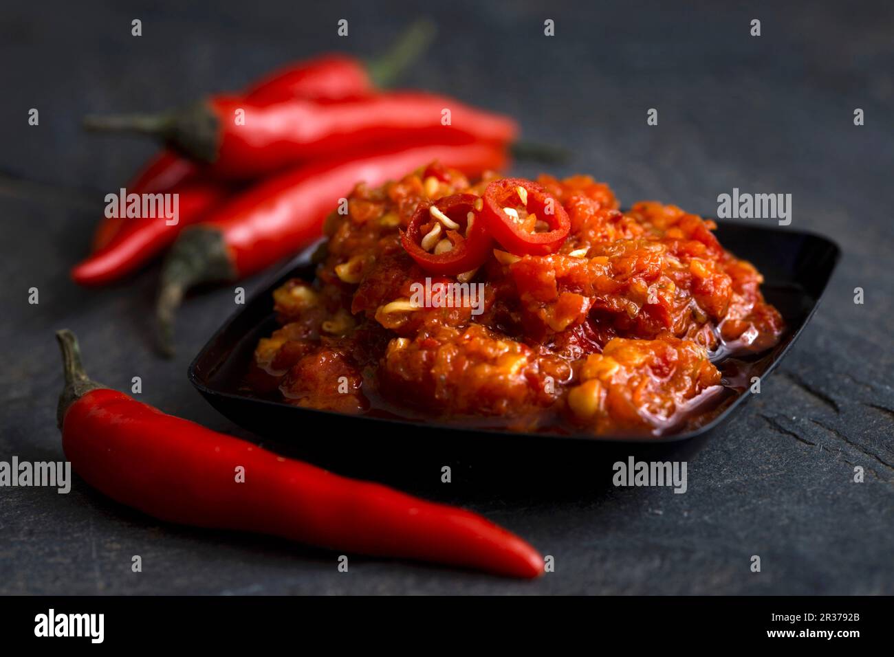 Black plastic dish with chilli paste in olive oil with fresh whole birds-eye chillies Stock Photo