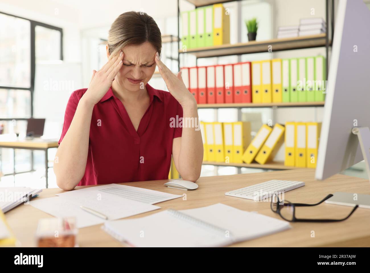 Suffering woman massages temples with hands sitting at desk Stock Photo ...