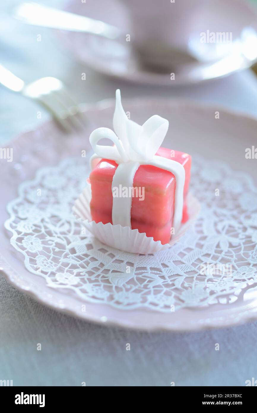 A pink petit four on a paper doily Stock Photo