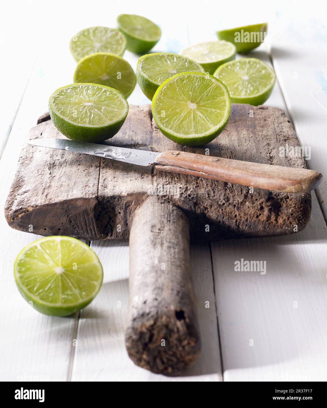 Halved limes on an old wooden board with a knife Stock Photo