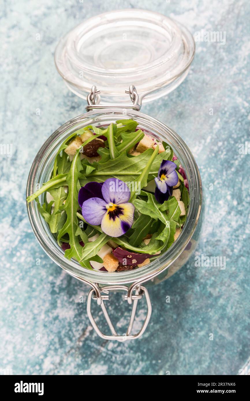 Quinoa salad with lambs lettuce, radicchio, rocket, croutons, goat's cheese and horned violets in a glass jar Stock Photo