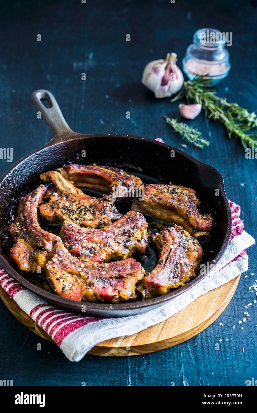 Pork ribs in a pan with garlic and fresh herbs Stock Photo