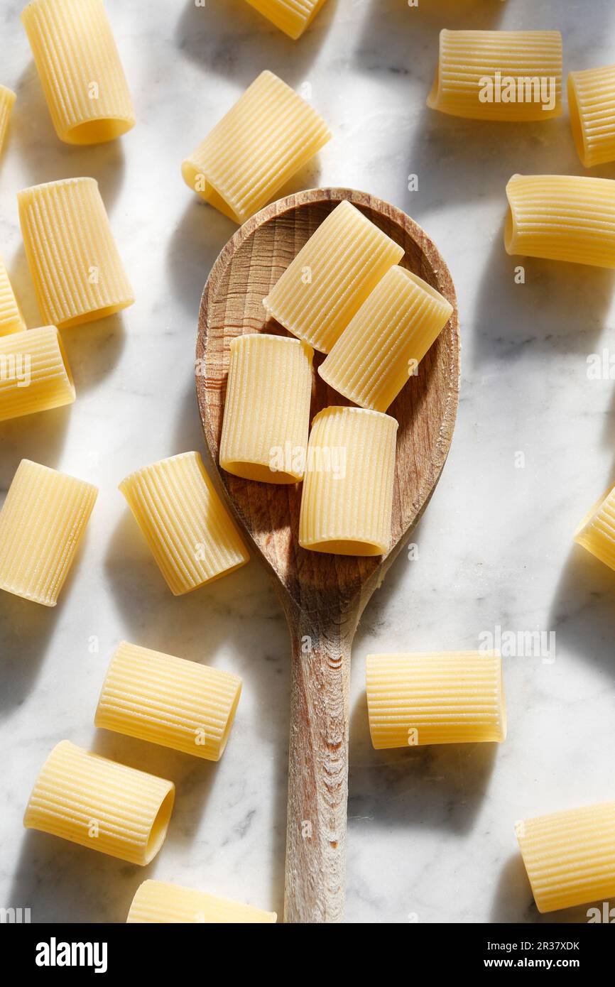 Mezze Maniche (cylindrical pasta) on a wooden spoon and marble background (seen from above) Stock Photo