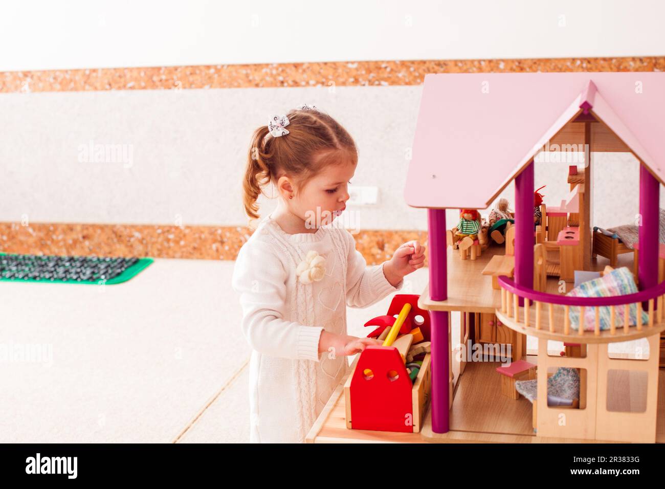 Pretty girl repairs the roof of dollhouse in the kindergarten Stock