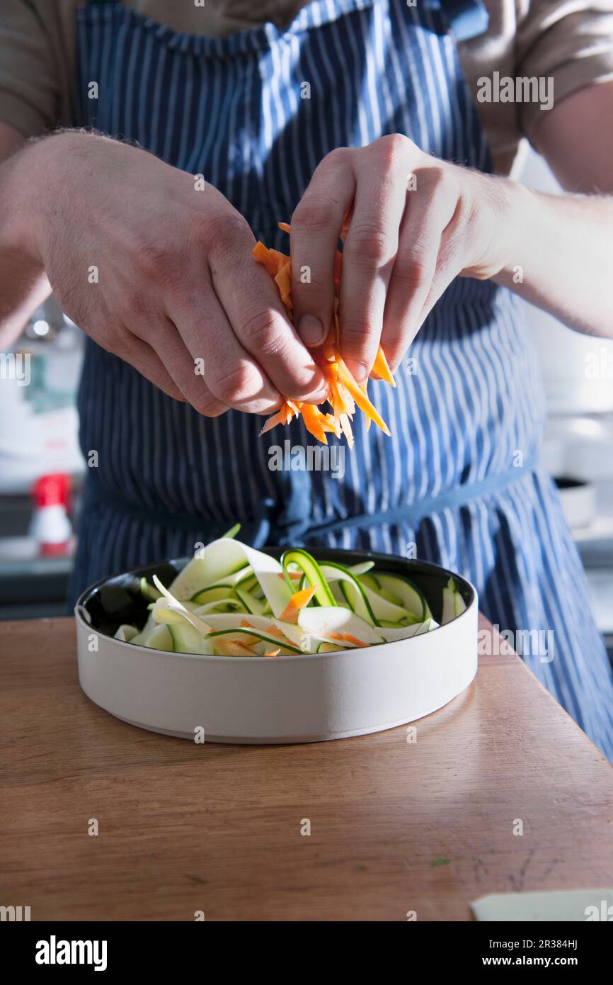 A man scattering julienne carrots over a vegetable salad Stock Photo