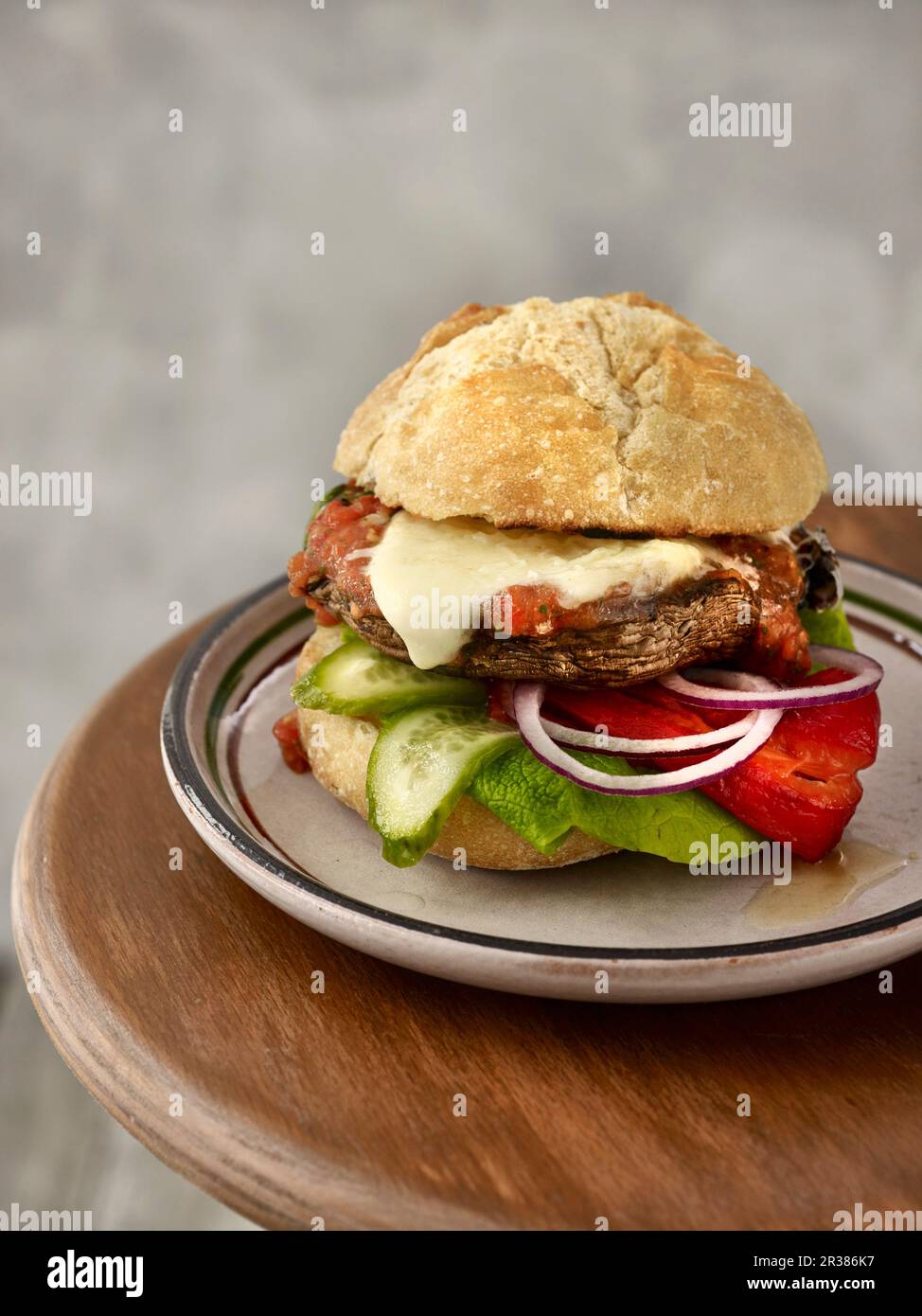 A portobello burger with grilled peppers, cucumber slices, red onion rings, mozzarella, and tomato and pepper salsa Stock Photo