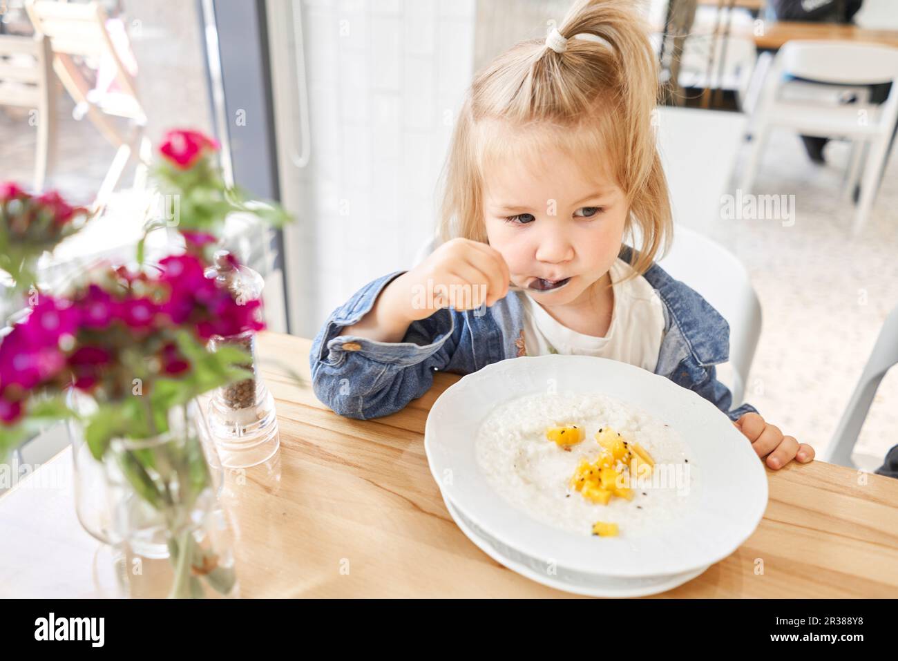Cute little girl drinking eating rice porridge with mango. enjoying ...