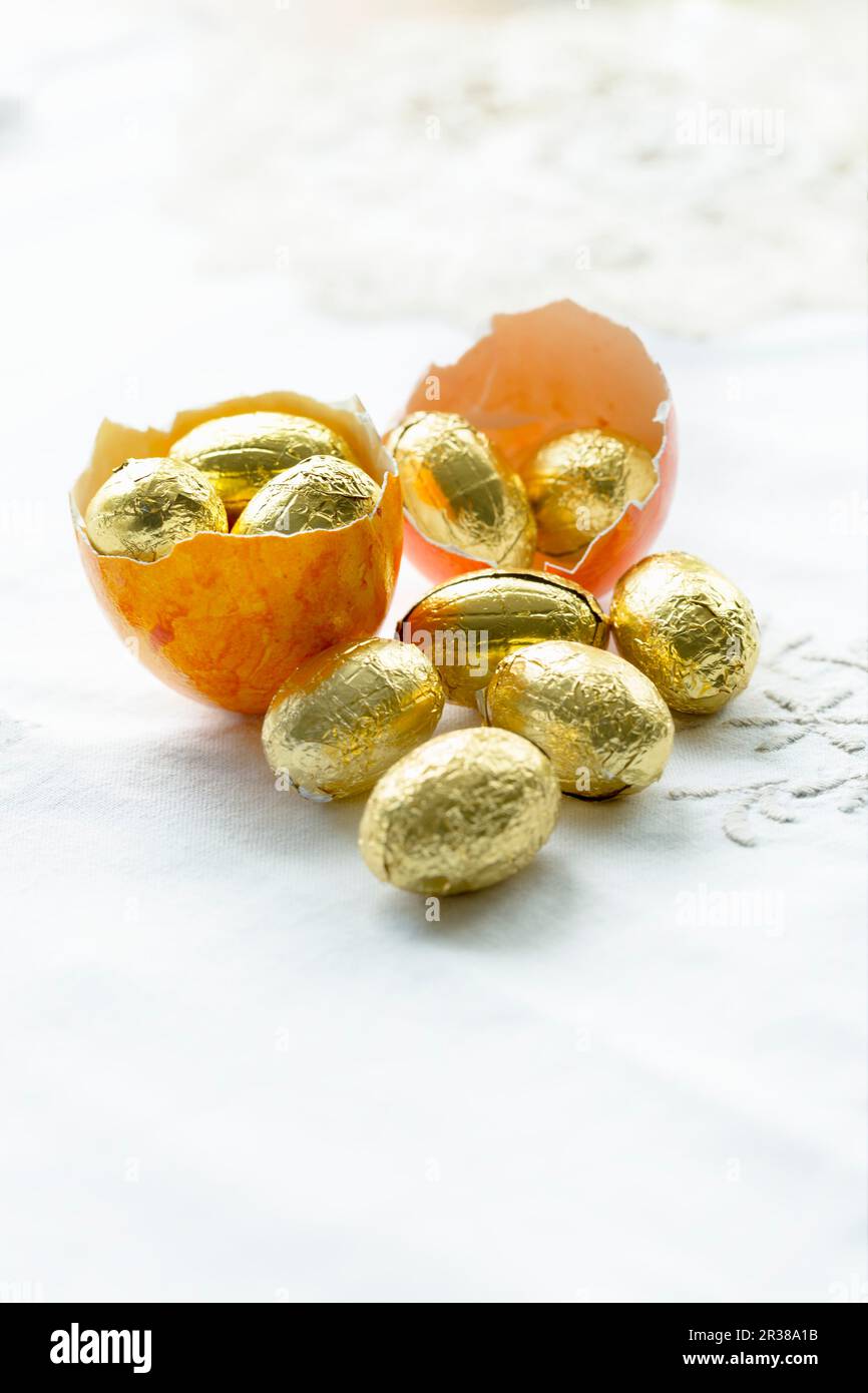 A dyed egg shell of an empty Easter egg filled with chocolate eggs wrapped in gold foil Stock Photo