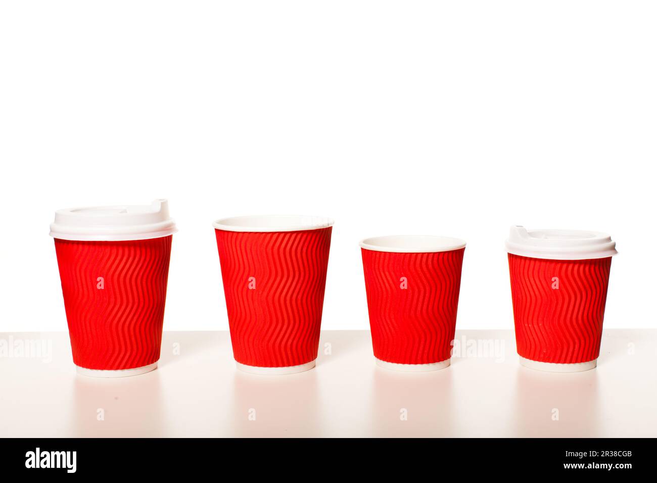 Disposable red paper coffee cups of different sizes standing in a row on a white background