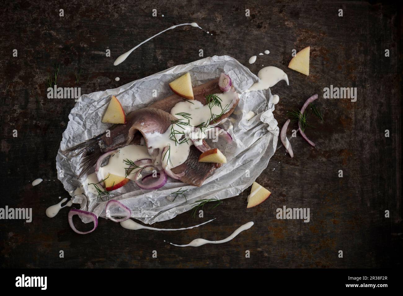 Herring fillets with yoghurt sauce, pieces of apple, shallots, and dill on parchment paper Stock Photo