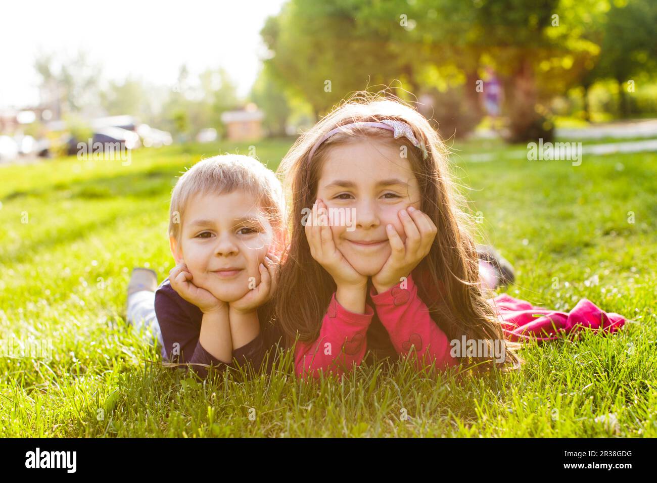 Picture of brother and sister having fun in the park, two cheerful children laying down on green