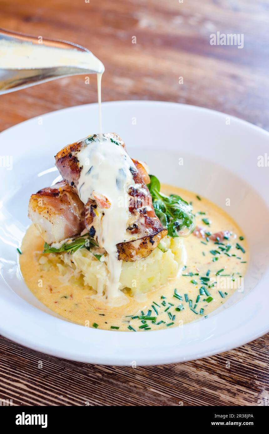 Sea bass fish fillets wrapped in bacon on a potato mash with spinach