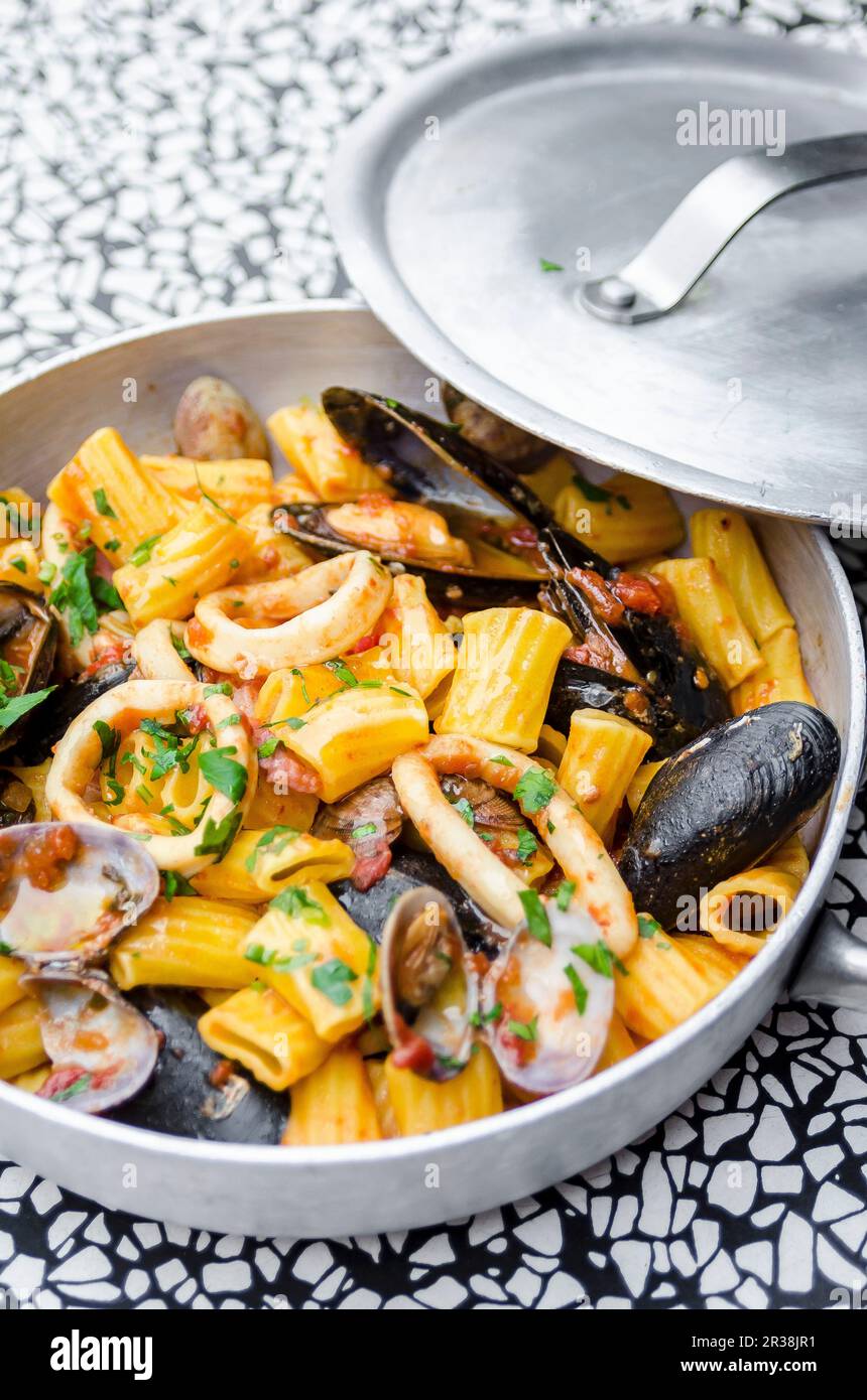 Mezze maniche rigatoni pasta with seafood, calamari, squid, mussel, clams, cockles, parsley, tomato sauce Stock Photo