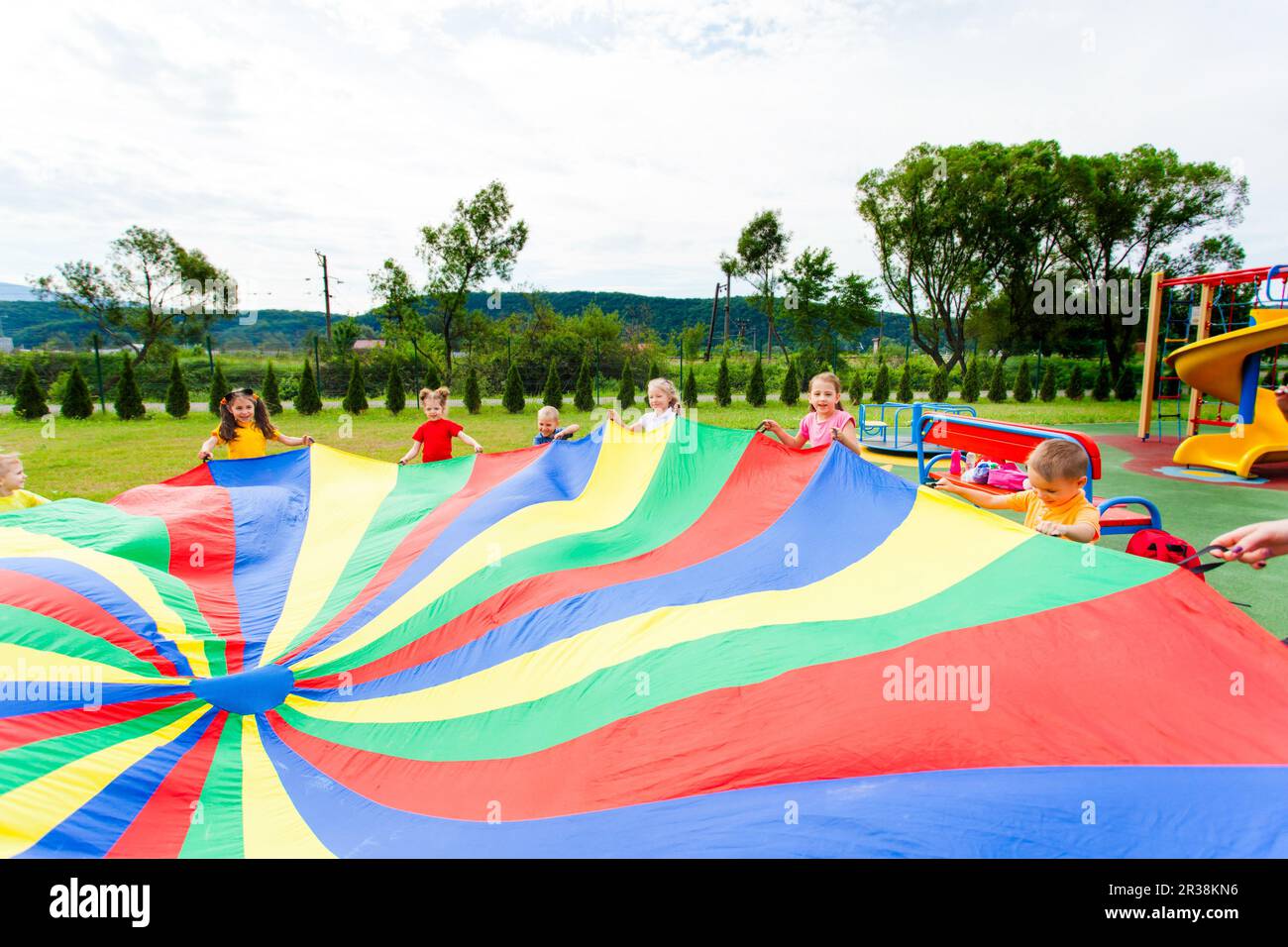 Rainbow parachute waived by kids in the summer outdoors Stock Photo