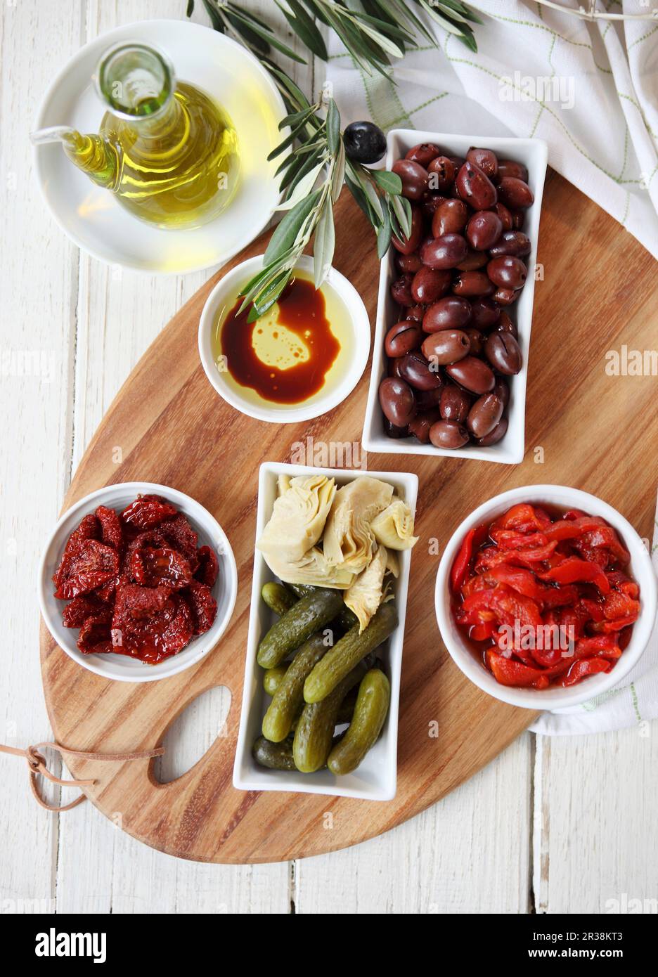 Antipasto dish - sun-dried tomatoes and capsicum, kalamata olives, gherkins, artichokes, Bread rolls, olive oil (with balsamic vinegar)and olive branc Stock Photo