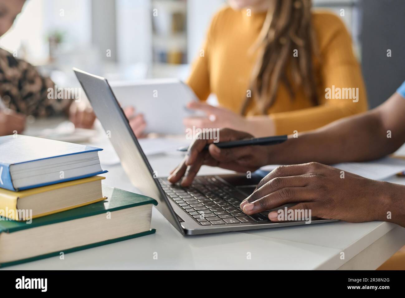 Close-up of student typing on laptop and doing task online while sitting at desk with other students during lesson Stock Photo