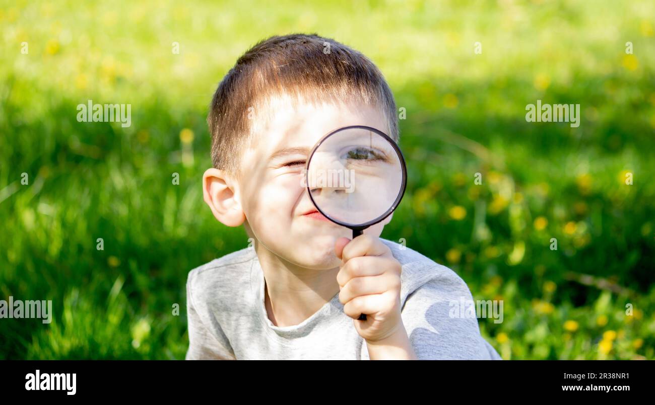 the boy looks at the flower through a magnifying glass. selective focus Stock Photo