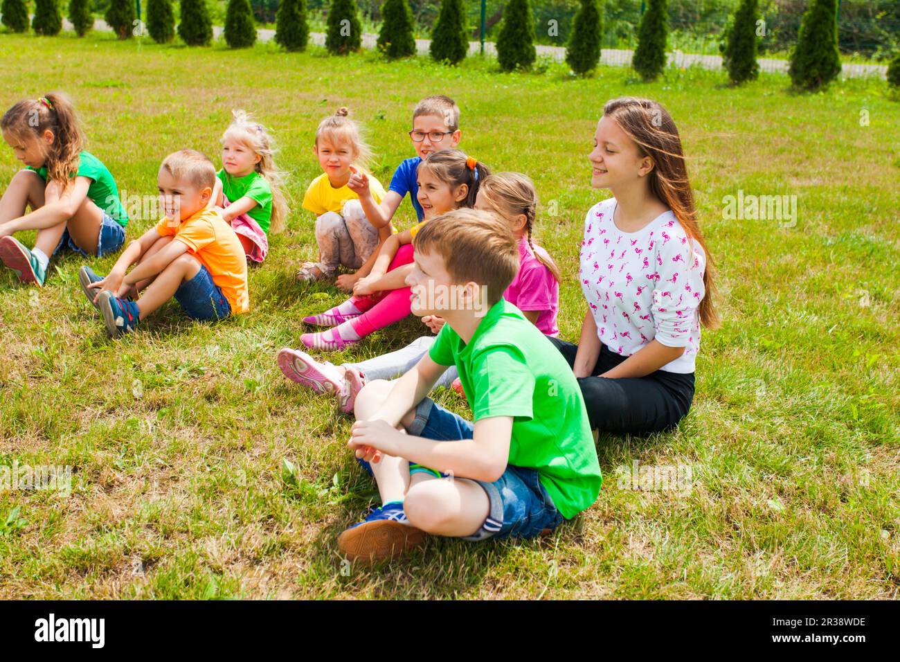 Smiling children sitting on a grass at outdoor lesson Stock Photo - Alamy