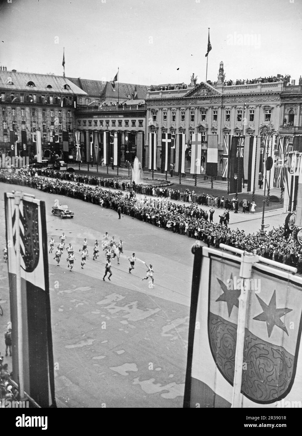 Berlin Olympics 1936. The 1936 Summer Olympics (German: Olympische Sommerspiele 1936), officially known as the Games of the XI Olympiad (German: Spiele der XI. Olympiade) and commonly known as Berlin 1936, were an international multi-sport event held from 1 to 16 August 1936 in Berlin, Germany.  Pictured the olympic flame being transported to the Olympiastadion in Berlin by runners on Pariser strasse in Berlin, about to pass Brandenburger Tor. This ceremony is called Olympic torch relay. Stock Photo