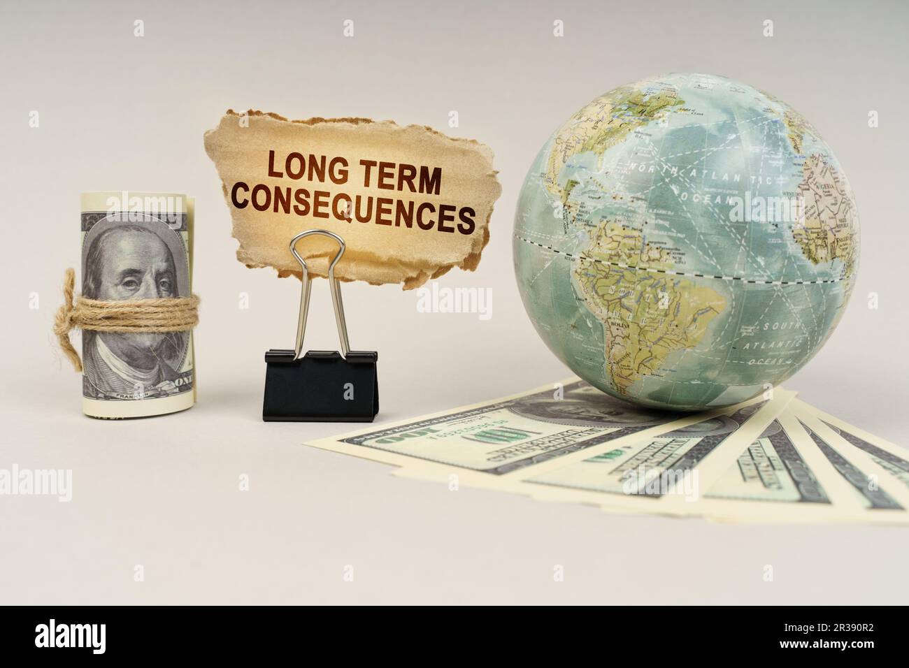 Business and finance concept. On the table are dollars, a globe and there is a sign with the inscription - Long Term Consequences Stock Photo