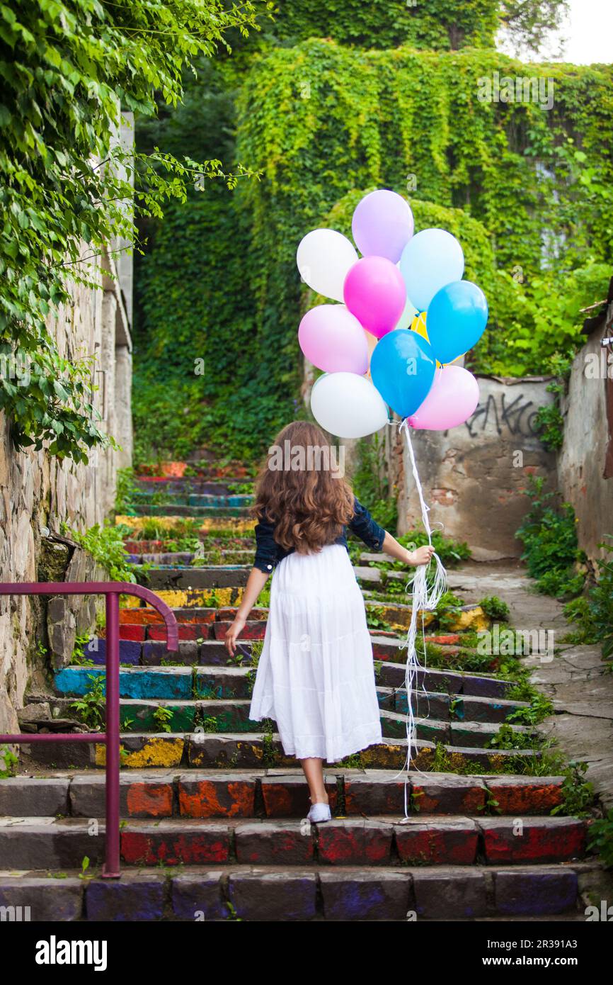 Girl is running with colorful balloons outdoors Stock Photo