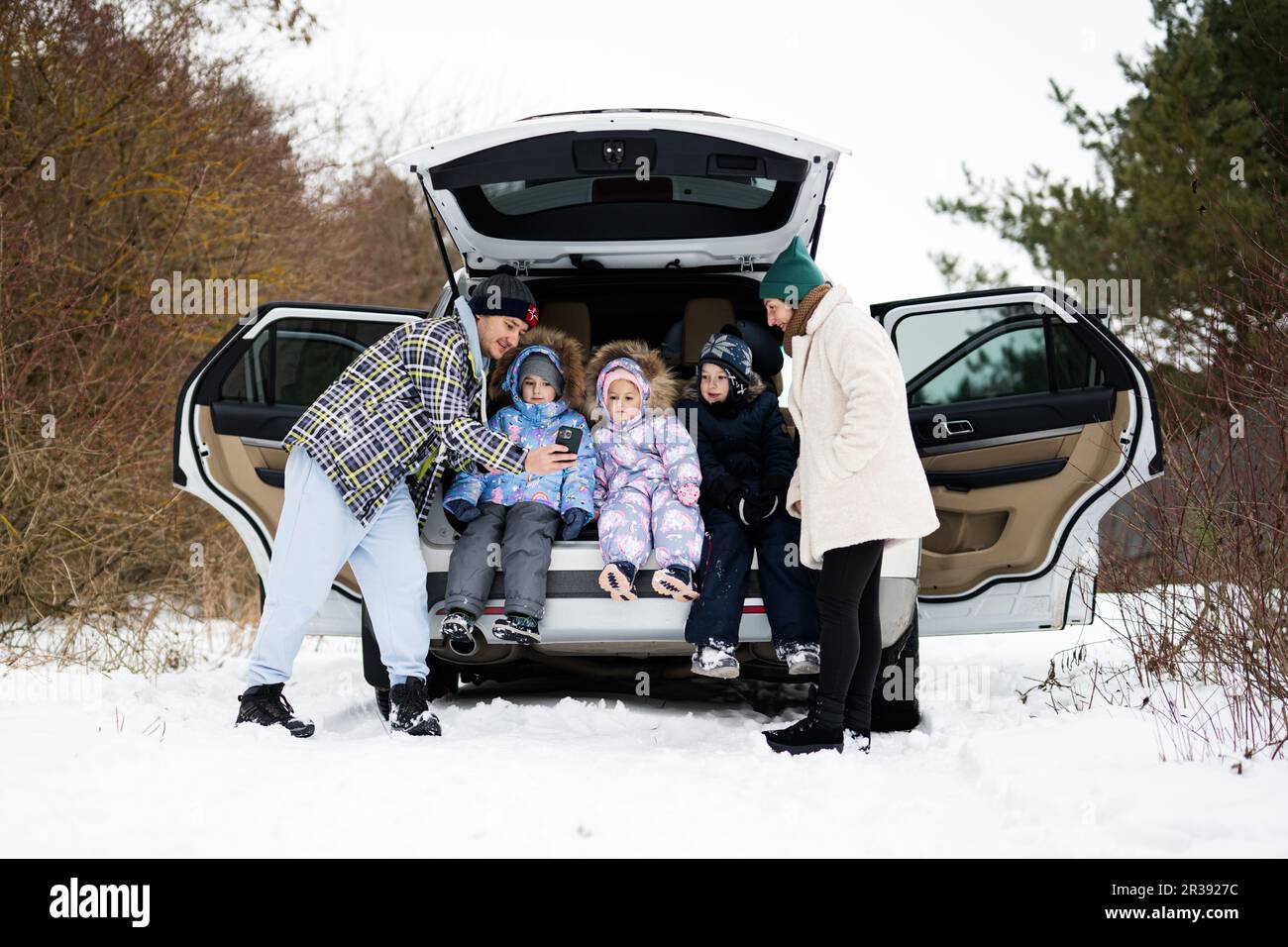 Family with kids sit on car suv with open trunk stand in winter forest ...