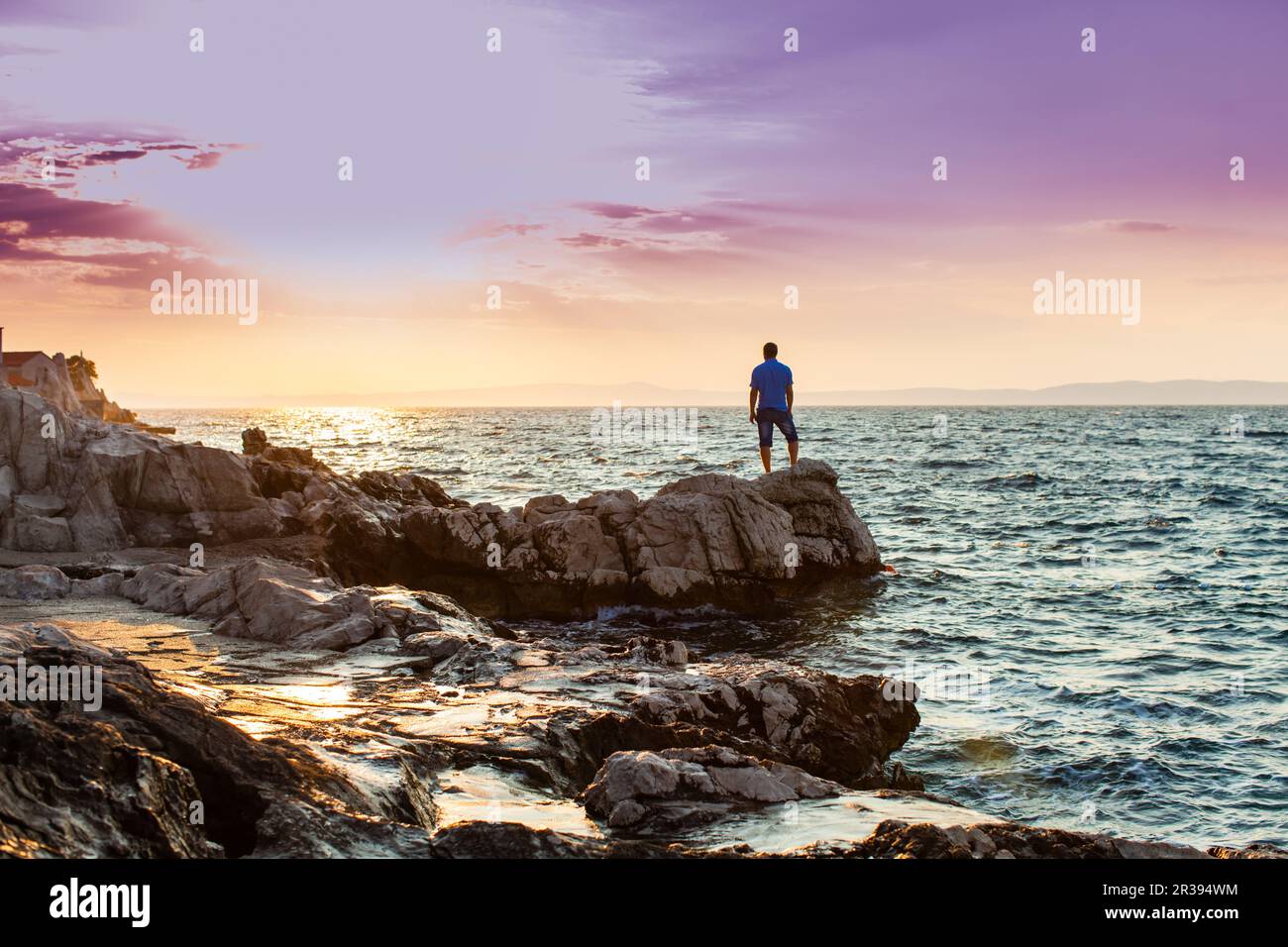 Yung man standing on a rock and looking at the sea sunset Stock Photo