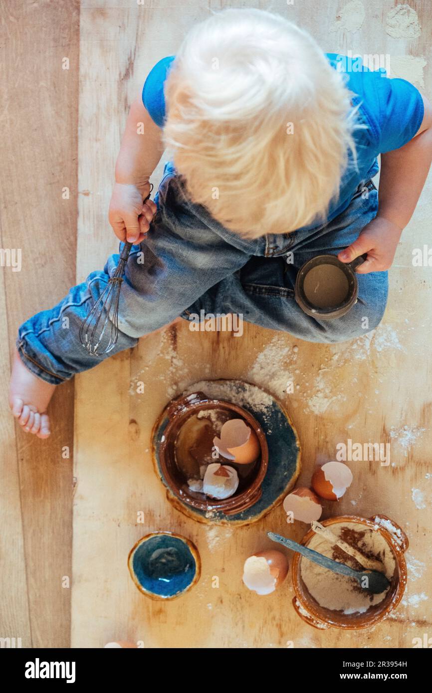 Child helping with cooking. Ingredients eggs, egg shels and flower. Stock Photo