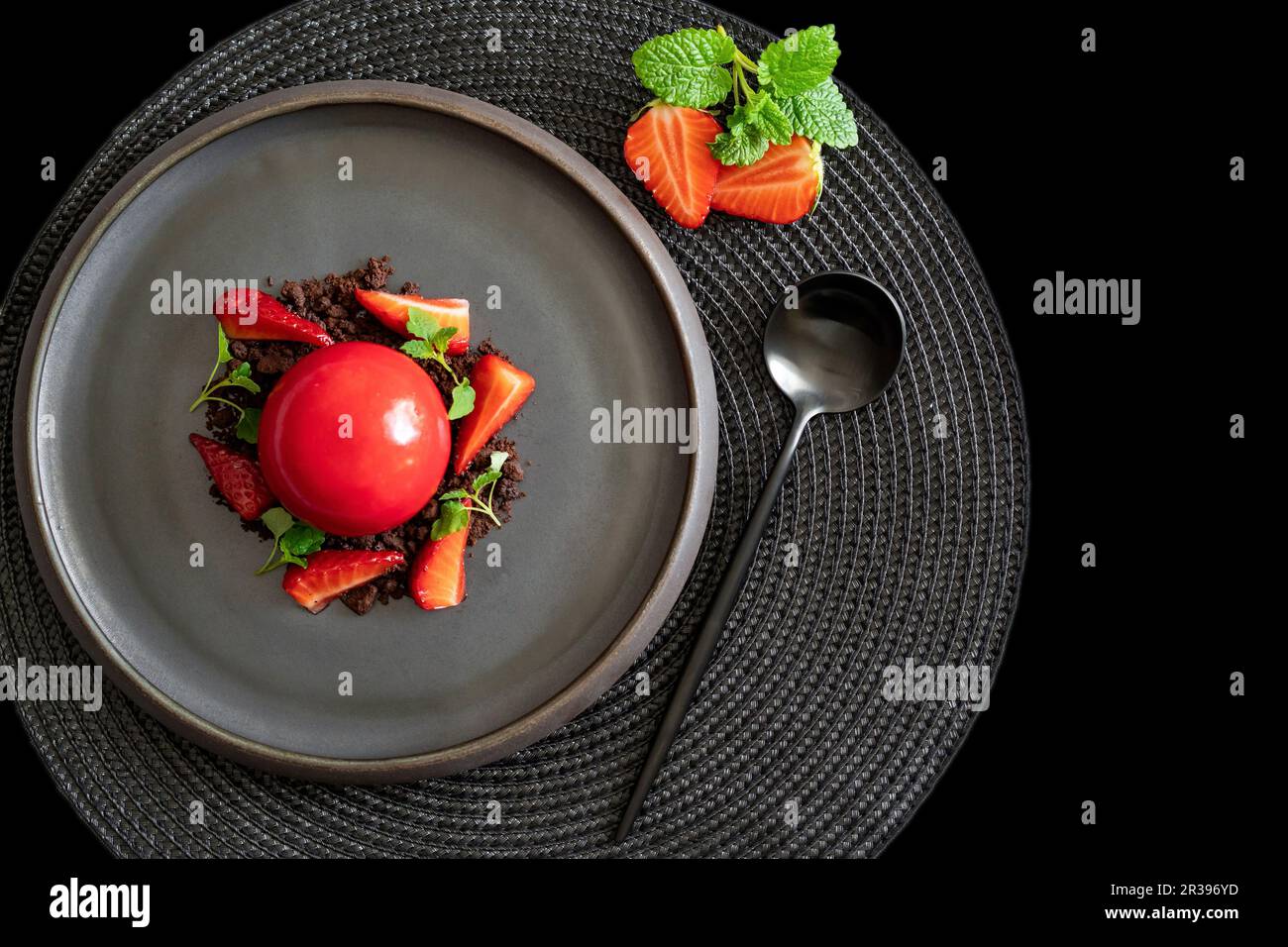 Top view of a sphere curd cake with strawberries and brownies. Dessert with smooth surfaces and mirror glaze on the black plate. Black background. Stock Photo