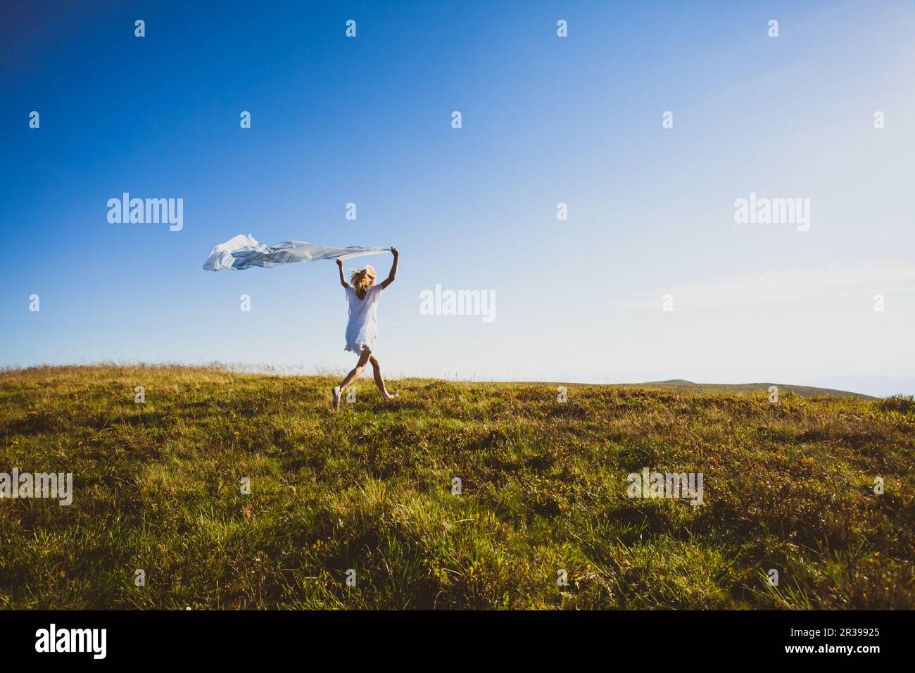Woman run with white textile high up in the mountains Stock Photo