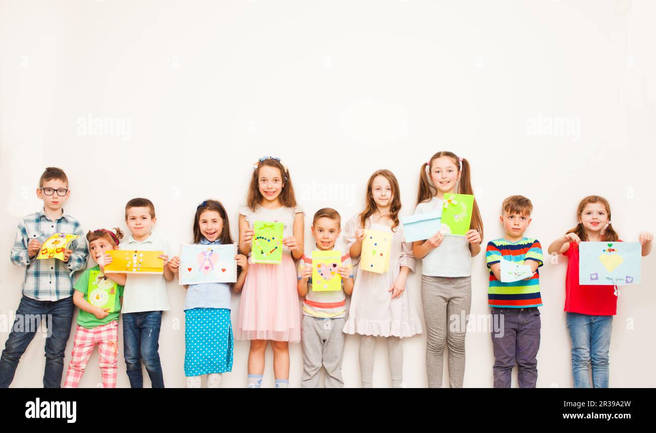 Happy kids showing their greeting card over white wall. Handmade paper crafts for kids Stock Photo