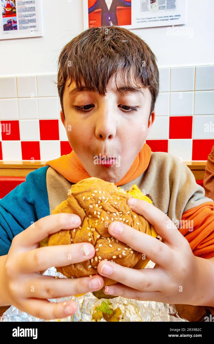 A boy eating a cheeseburger at a Five Guys Fast Food restaurant Stock