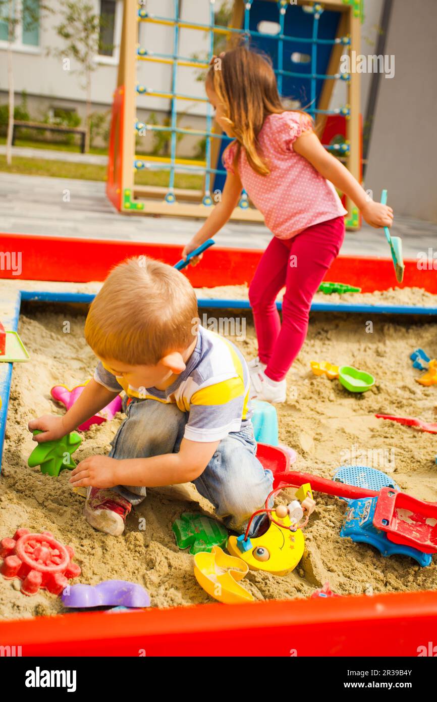 Happy children sitting in sandbox playing with plastic colorful toys. Stock Photo