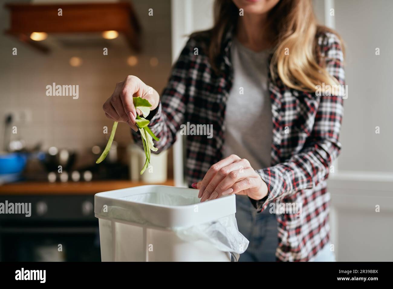 Female person throwing organic food waste in a compost bin. Responsible woman recycling cucumber