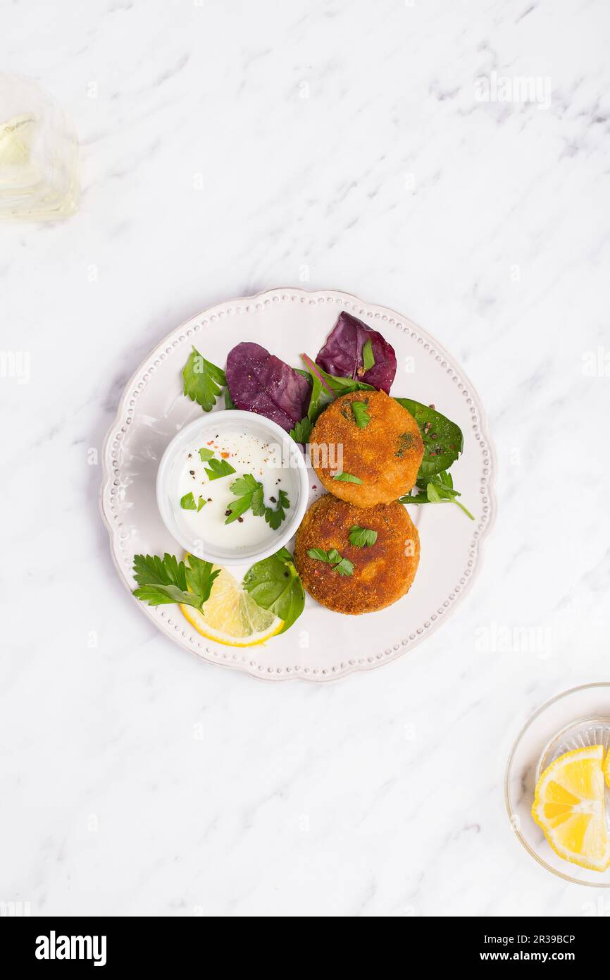 Fish patties on a white plate served with greek yogurt, lemon and fresh herbs Stock Photo