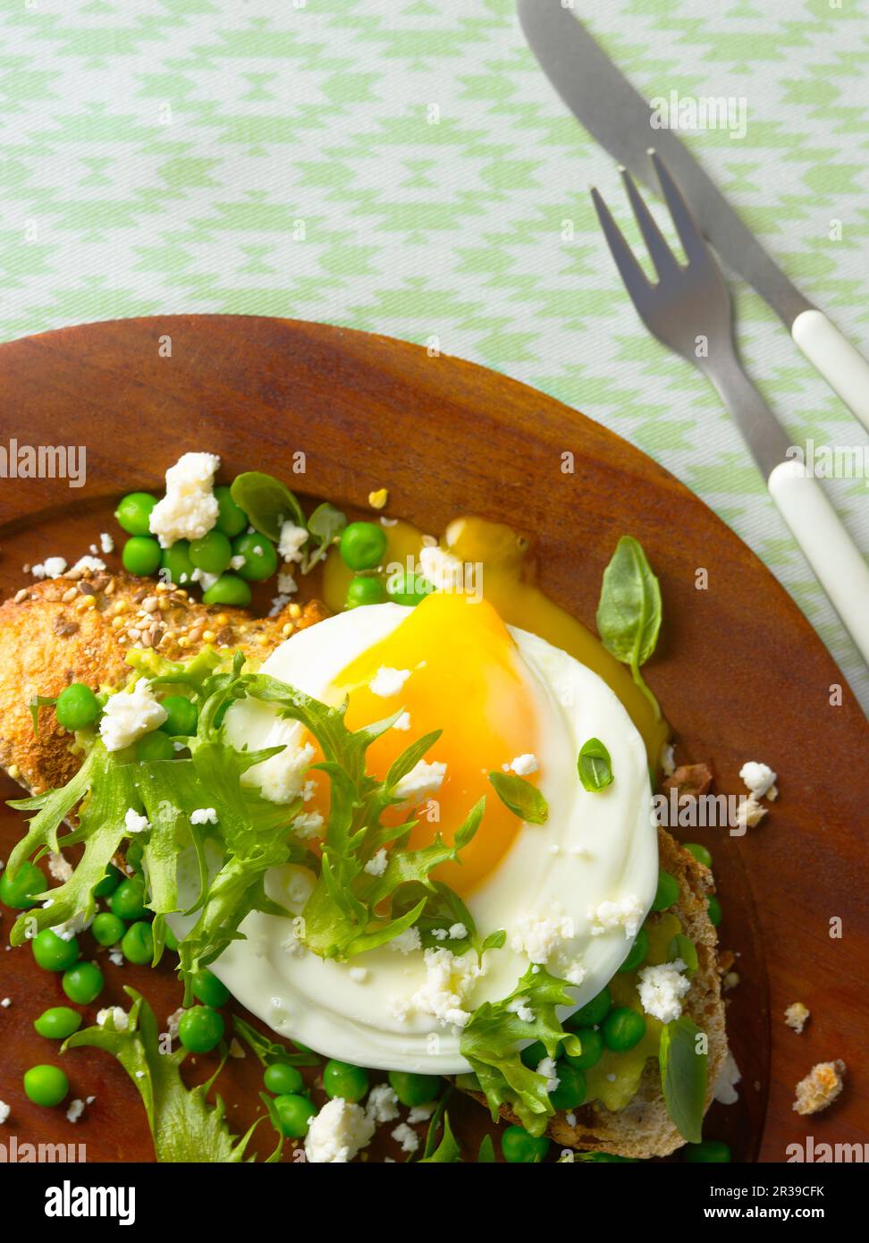 A fried egg on a slice of bread with peas, frisee salad and feta cheese Stock Photo