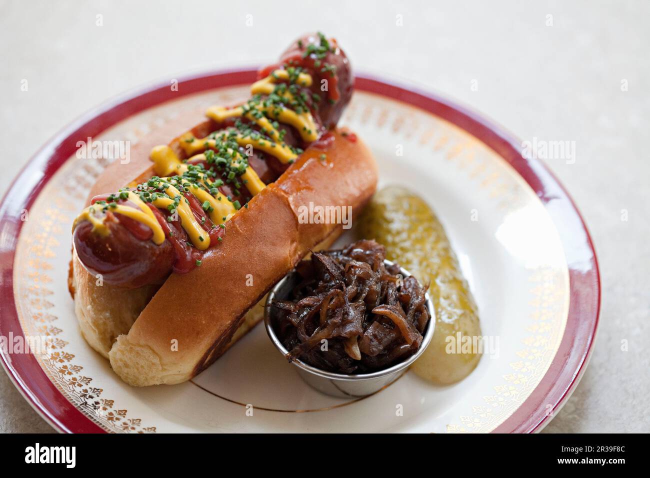 Hot dog covered in mustard and ketchup in a roll with a gherkin and