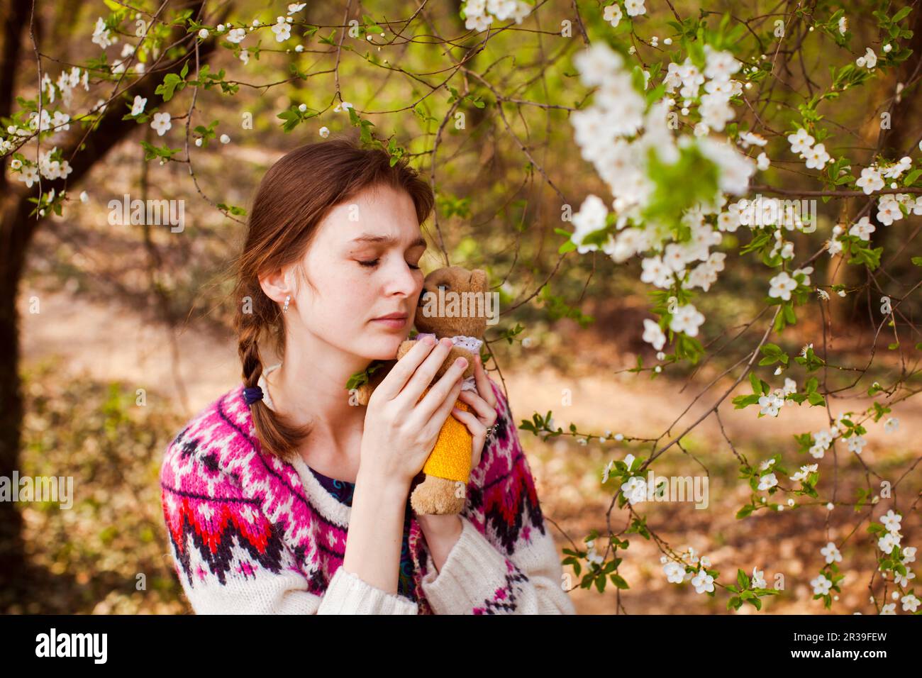 Teenage girl huggs toy bear in spring garden. Beautiful sad girl face ...